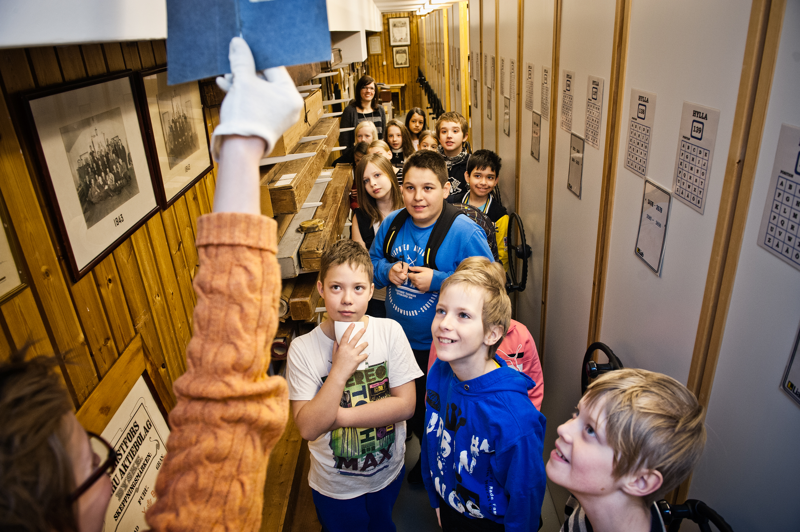 Fotografi utav barn på besök i arkivet, de tittar på en en handling som arkivpedagogen håller upp (med bomullshandksar!)