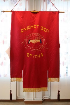 Fotografi utav rött standar med tofsar och texten "Enighet ger styrka"